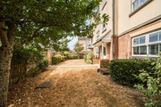 Communal outdoor space alongside the apartment building with mature trees, shrubs, and a pathway running through the grounds.