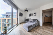Living space with wall art, sofa beside floor-to-ceiling windows and a door leading into a hall.