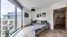 Living space with wall art, sofa beside floor-to-ceiling windows and a door leading into a hall.
