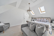 Loft bedroom with double bed, skylights, seating area and hanging ceiling light.