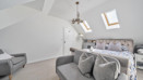 Loft bedroom with double bed, skylights, seating area and hanging ceiling light.