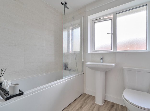 Family bathroom with bathtub, sink, toilet, and frosted window on a white wall.