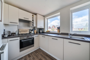 Kitchen with white cabinets, oven, hob, and window overlooking nearby buildings.