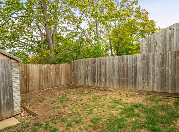 Enclosed rear garden with wooden fencing and trees behind fence.