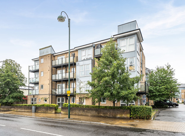 Apartment building with balconies, trees and parking area.