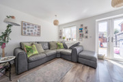 A white painted living room with grey corner sofa, pictures on the wall and patio doors to the right