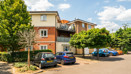 Apartment building with parked cars and trees in a shared parking area.