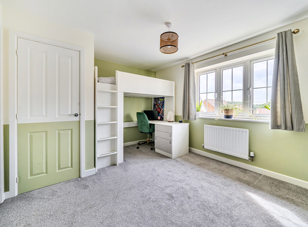Bedroom with bunk bed, desk, window and carpeted floor.
