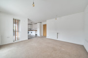 Open-plan living area with carpeted floor and kitchen in the background.