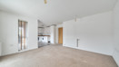 Open-plan living area with carpeted floor and kitchen in the background.