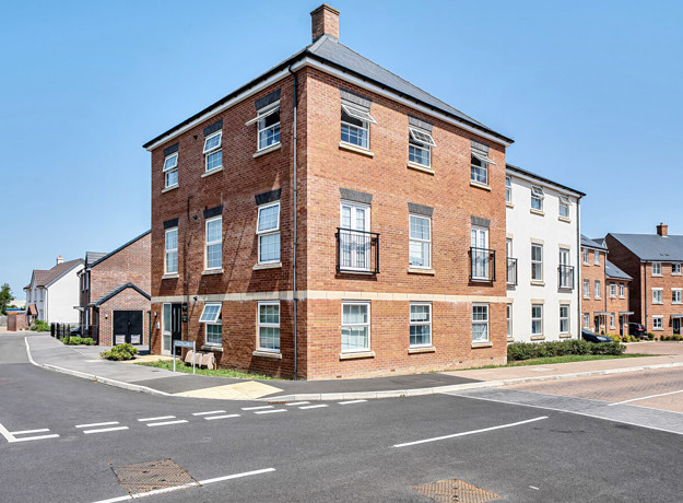 Red brick apartment building on a street corner with nearby residential homes.