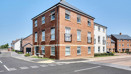 Red brick apartment building on a street corner with nearby residential homes.