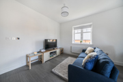 Living room with blue sofa, TV stand, rug, window, and grey flooring throughout.