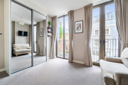Bedroom with mirrored wardrobe doors and windows opening onto a balcony.