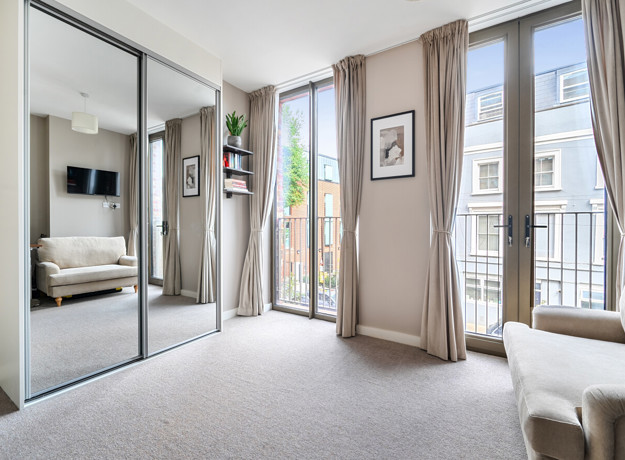 Bedroom with mirrored wardrobe doors and windows opening onto a balcony.