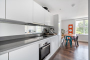 White galley kitchen with integrated appliances and dining area beyond.
