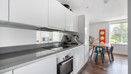 White galley kitchen with integrated appliances and dining area beyond.