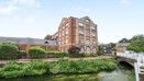 Brick building beside a canal with greenery and a nearby bridge.