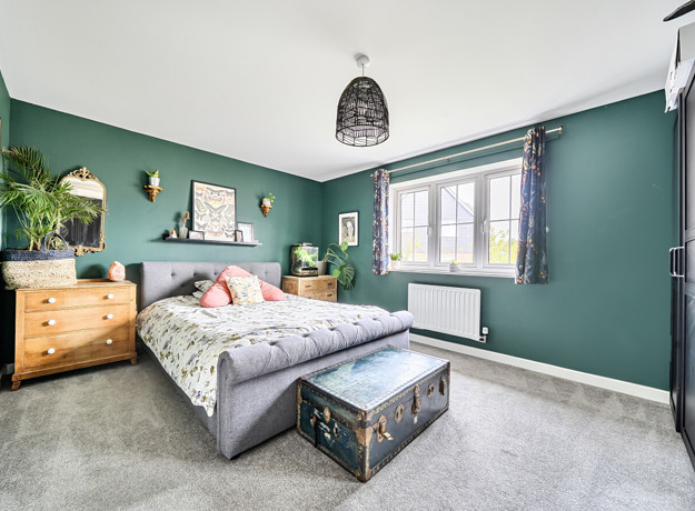 Bedroom with double bed, chest of drawers, window and green walls.
