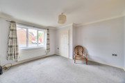 Empty living room with large window, beige carpet, and a single chair by the wall.