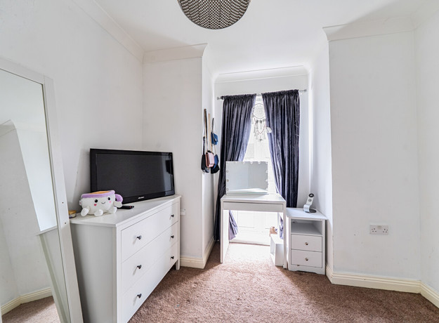 Bedroom with chest of drawers, vanity table, mirror, desk and window.