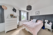 Bedroom with double bed, dresser, bedside tables with lamps and grey curtains by window.