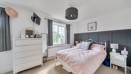 Bedroom with double bed, dresser, bedside tables with lamps and grey curtains by window.