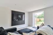 Living room with dark sofa, wall-mounted TV, and glass door opening to a garden.