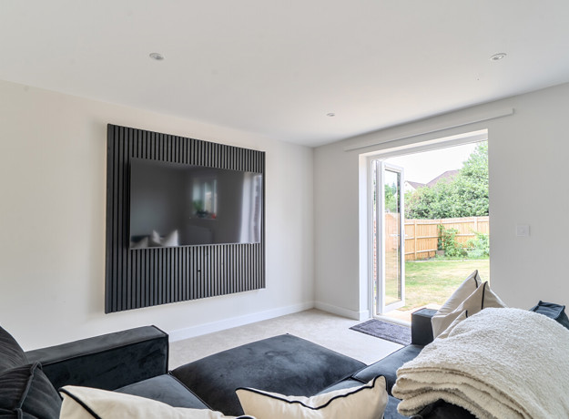 Living room with dark sofa, wall-mounted TV, and glass door opening to a garden.