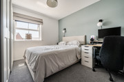 Bedroom with double bed, desk, chair, and wardrobe beside a window.