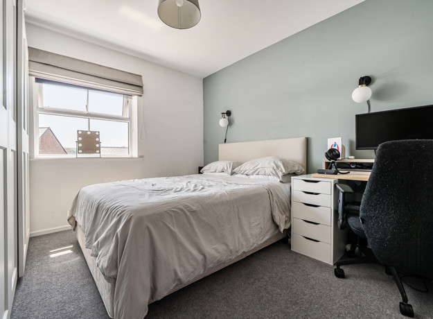 Bedroom with double bed, desk, chair, and wardrobe beside a window.