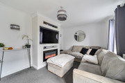 Living room with corner sofa, footstool, fireplace, television and shelving.