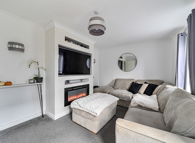 Living room with corner sofa, footstool, fireplace, television and shelving.